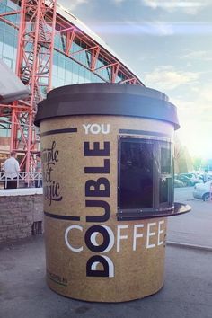 a coffee cup sitting on top of a sidewalk next to a tall building with a sign