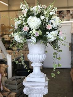 a white vase filled with lots of flowers on top of a pedestal in a store