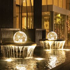 two water fountains in front of a building at night