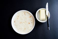 a white bowl filled with food next to a knife and butter container on a black surface