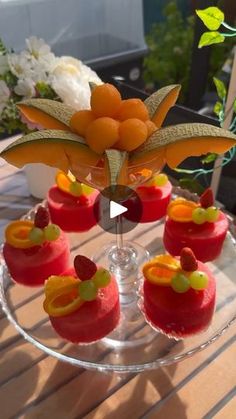 small desserts are arranged on a clear platter with flowers in the back ground