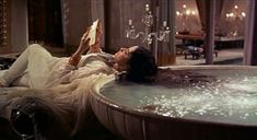 a woman laying in a bathtub with her feet up on the floor while reading a book