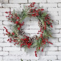 a christmas wreath on a brick wall with pine cones and red berries