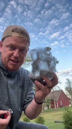 a man is holding something in his hand and looking at the camera while sitting outside