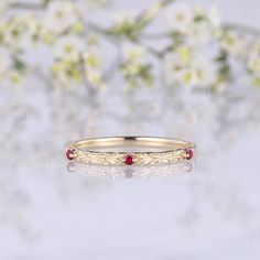 a gold ring with two red stones on it and flowers in the background, sitting on a white surface