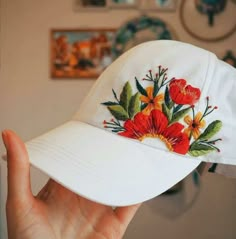 a white hat with red and yellow flowers embroidered on the brim, held up by a person's hand