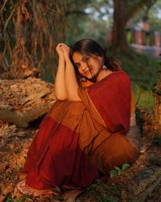 a woman sitting on the ground in a red and brown sari with her hands behind her head