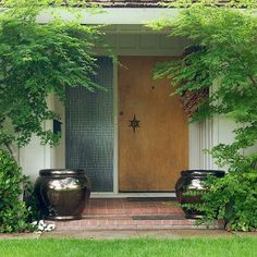 two planters sitting in front of a door on the side of a house next to trees