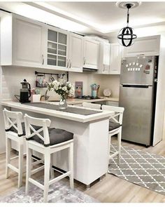 a white kitchen with an island and stools next to the refrigerator freezer in it