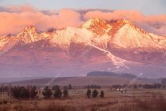 the mountains are covered in snow as the sun is setting on them, and some clouds are