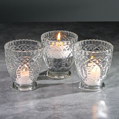 three clear glass candlesticks sitting next to each other on a gray table top