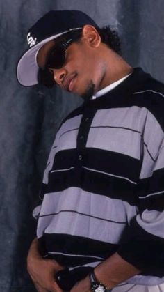 a man wearing a hat and sunglasses standing in front of a wall