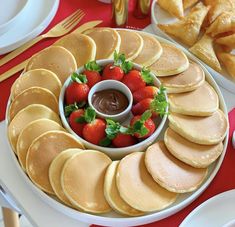 pancakes and strawberries are arranged on a plate with chocolate sauce in the center, along with other plates