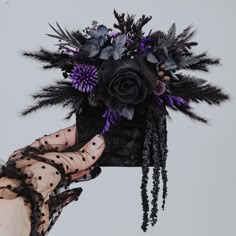 a hand holding a black and purple flower arrangement