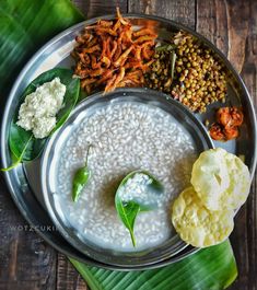 a metal plate topped with different types of food on top of a wooden table next to green leaves