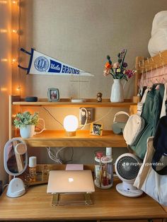 a laptop computer sitting on top of a wooden desk next to a shelf filled with clothes