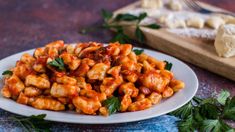 a white plate topped with pasta covered in sauce and garnished with parsley