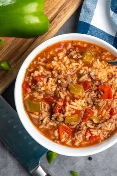 a white bowl filled with chili and rice next to a knife on top of a cutting board