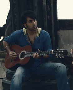 a man sitting on a chair holding a guitar in his hand and looking at the camera