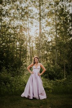 a woman is standing in the woods wearing a purple dress and posing with her hands on her hips