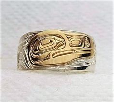 On offer is a made to order West Coast Namgis First Nation Hand carved sterling silver with 14k gold overlay ''Raven'' ring. by World renowned master carver Joe R. Wilson with his depiction of Raven in the style of the Namgis, Kwakuitl First Nation. Initialed by Joe. Fine example of Indigenous Art from the Northwest Coast First Nations of Canada. PLEASE NOTE THAT THIS IS A CUSTOM RECREATED HAND CARVED ITEM THAT WILL HAVE SLIGHT, SUBTLE DIFFERENCES THAT ARE VERY HARD TO DISTINGUISH WHEN COMPLETED Symbolic Carved Jewelry For Formal Occasions, Carved Symbolic Yellow Gold Jewelry, Yellow Gold Symbolic Carved Jewelry, Symbolic Carved White Gold Jewelry, Carved Gold Ring Jewelry, Adjustable Carved Jewelry For Anniversary, Symbolic Carved Gold Jewelry, Unique Carved Yellow Gold Ring, Ceremonial Sterling Silver Engraved Ring With Polished Finish