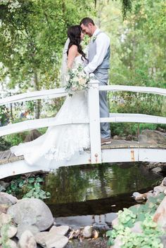 a bride and groom kissing on a bridge over a stream