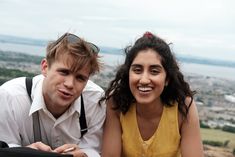 a man and woman taking a selfie on top of a hill with the city in the background