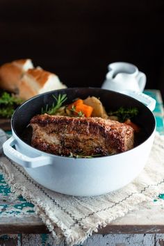 a pot roast with potatoes, carrots and meat in it on a wooden table