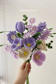 a hand holding a bouquet of purple and white flowers