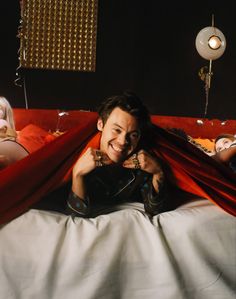 a man laying on top of a bed under a red blanket next to two women