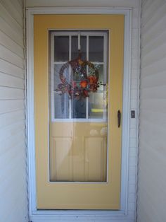 a yellow front door with a wreath on the window sill and glass pane