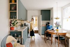 two people standing in a kitchen next to a dining room table with chairs and an open door