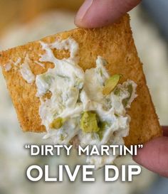 a hand holding a cracker that has some food on it and the words dirty martini olive dip