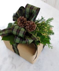 a present wrapped in plaid with pine cones and greenery sits on a marble table