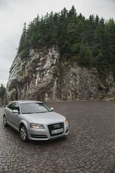 a silver car parked in front of a large rock formation on a cobblestone road