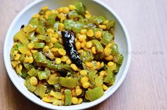 a white bowl filled with corn and green peppers on top of a wooden table next to a spoon