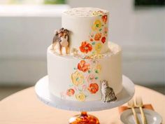 a three tiered cake decorated with cats and flowers on a table next to utensils