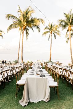 a long table set up with white linens under palm trees