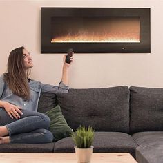 a woman sitting on a couch holding a remote in front of an electric fire place