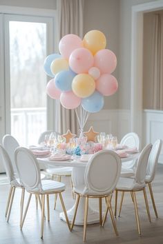 a bunch of balloons floating over a dining room table with white chairs and pink, blue, yellow and green decorations