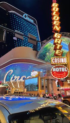 cars are parked in front of the casino and hotel at night with neon signs on the building