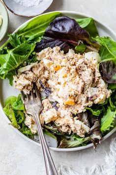 a salad with chicken and lettuce on a white plate next to a fork