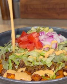 a bowl filled with lettuce, tomatoes and dressing being drizzled over it