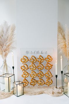 a table topped with candles and vases filled with gold pretzel cookies on top of a white surface