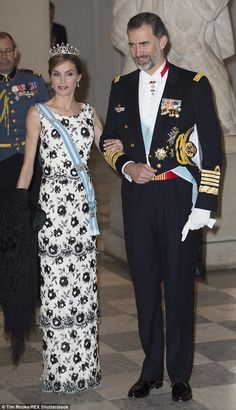 a man and woman standing next to each other in formal dress clothes, wearing tiaras