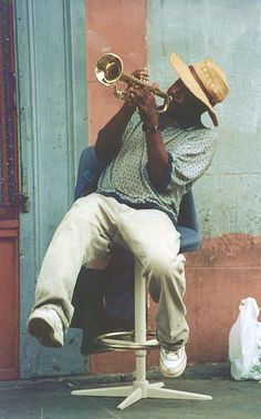 a man sitting on top of a stool playing a trumpet in front of a building