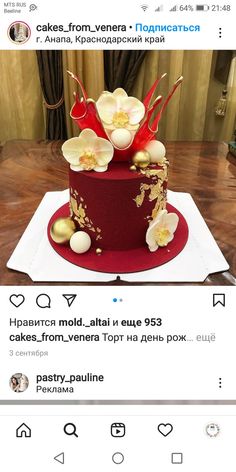 a red cake with white flowers and gold decorations on the top is sitting on a table