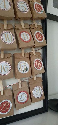 brown paper bags with red and white numbers are hanging from clothes pins in front of a black frame