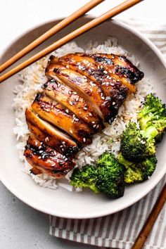 a white plate topped with meat and rice next to chopsticks