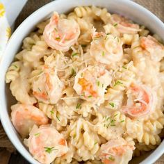 a bowl filled with pasta and shrimp on top of a wooden table next to a napkin